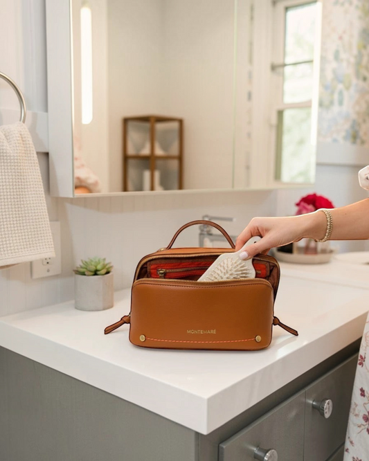 Montemaré Roma foldout toiletry case in tan vegan leather with orange accents, sitting on a bathroom vanity.