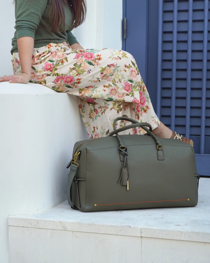 Montemaré Roma olive green vegan leather travel duffel bag with a tassel, sitting on a white step next to a woman.