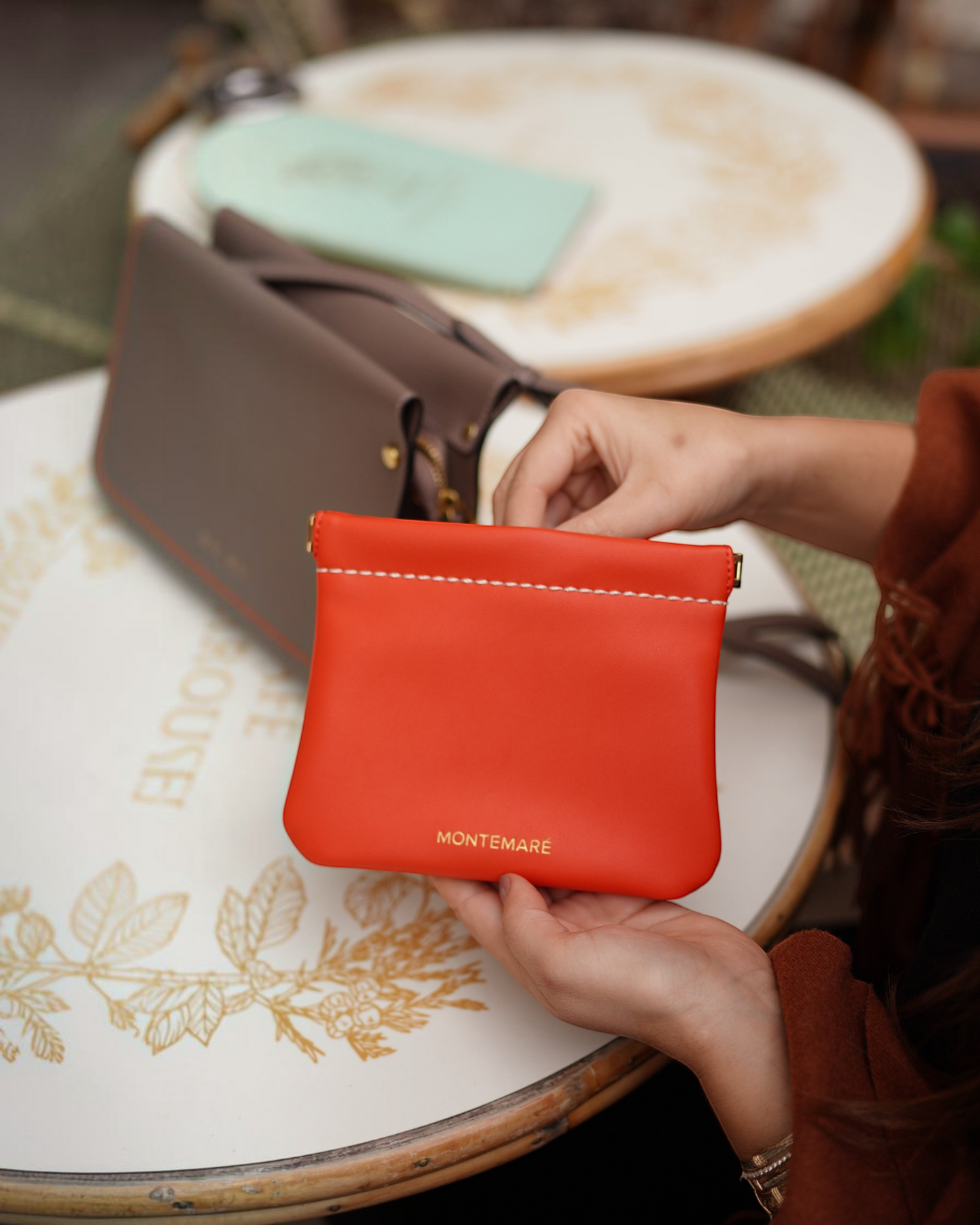 Montemaré Roma square pouch in vibrant orange vegan leather with a secure spring-frame closure held in hands.