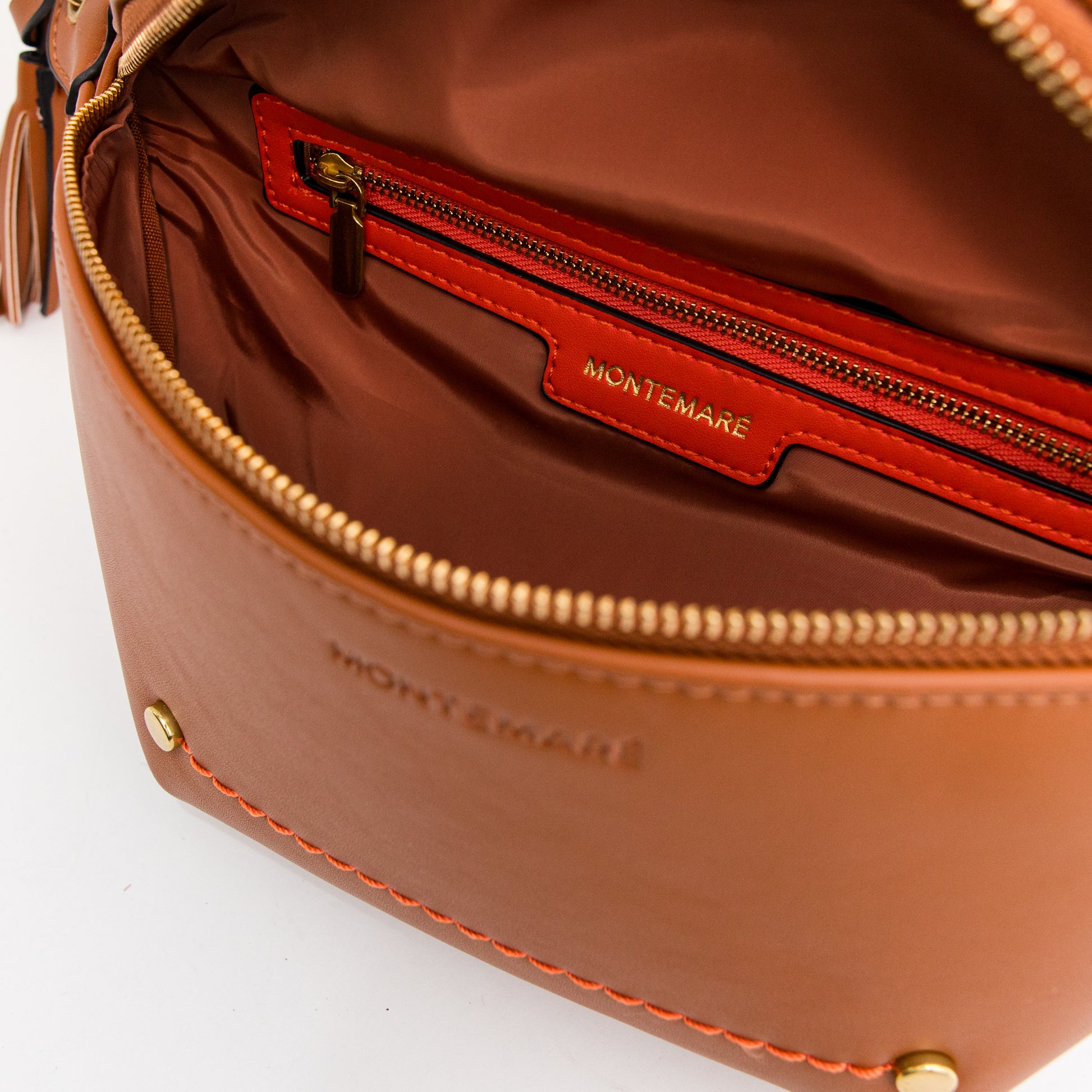 Brown vegan leather sling with orange trim interior pocket and brass-finished zipper, featuring 'Montemaré' branding.
