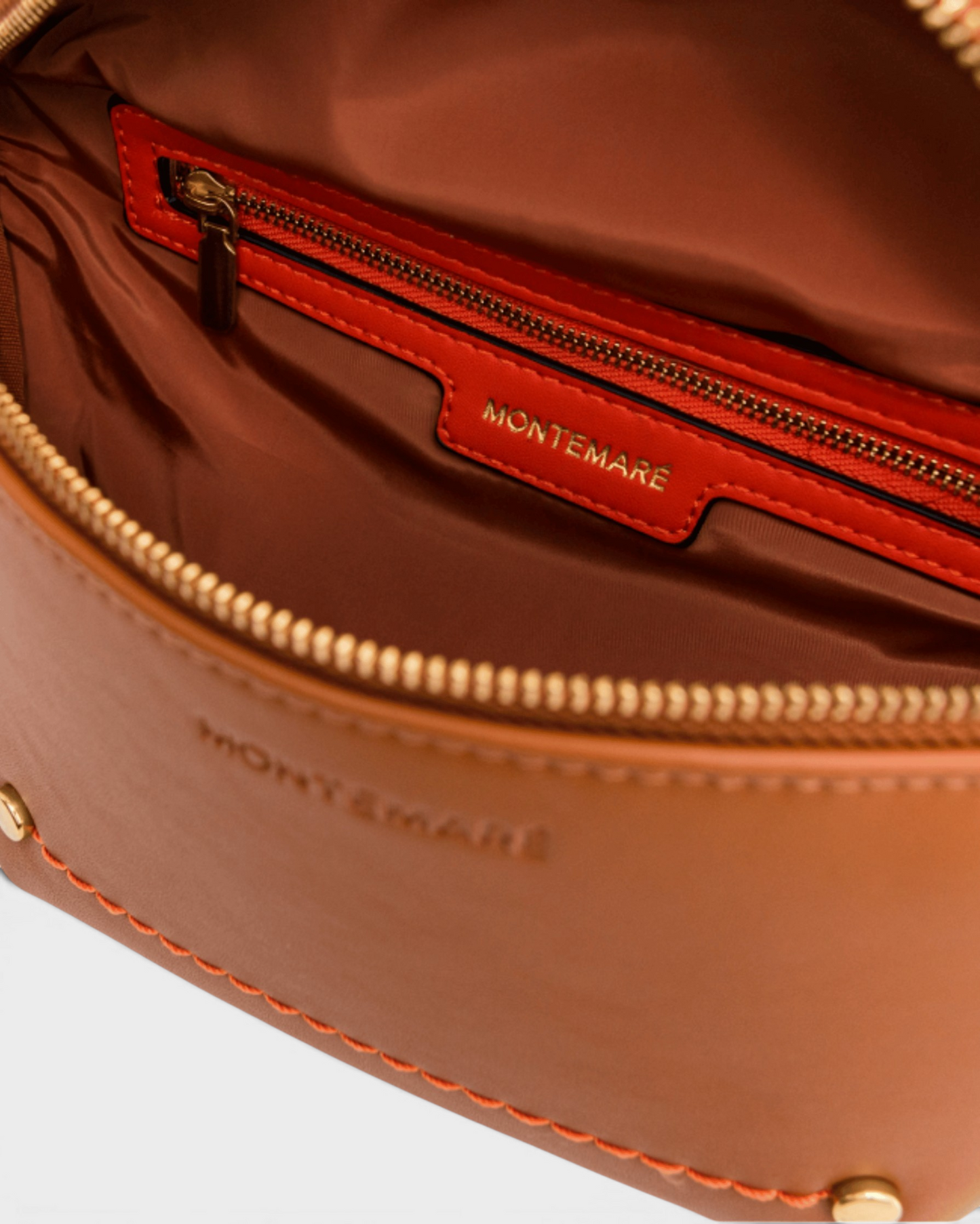 Interior of Montemaré Roma Sling bag in tan vegan leather with orange accents, gold zipper, and branded lining.