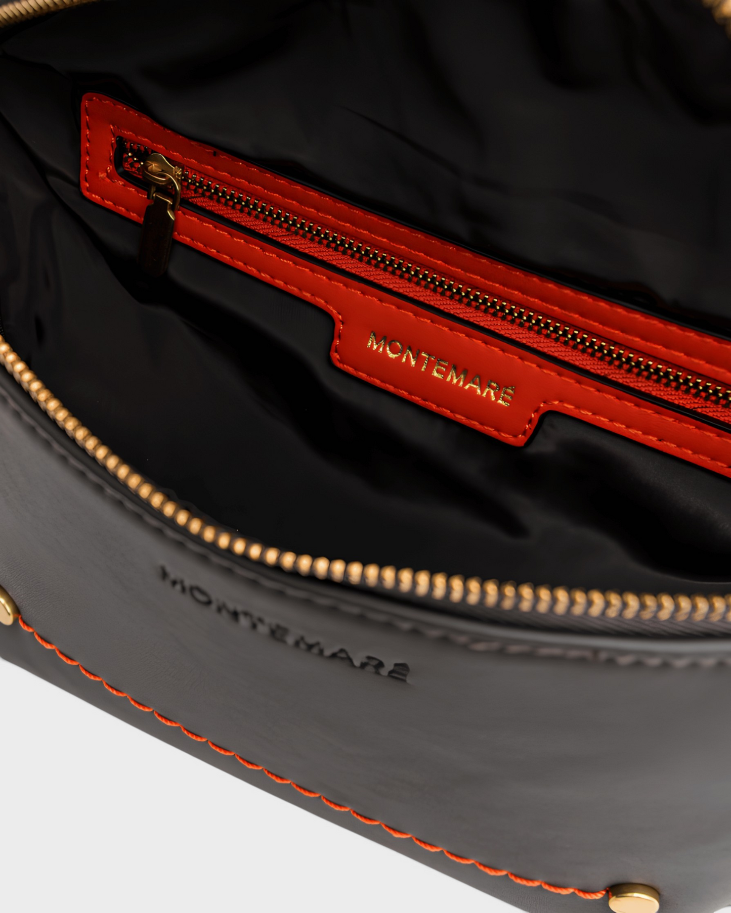 Interior of Montemaré Roma Sling bag featuring black vegan leather, orange trim, gold zippers, and brand logo.