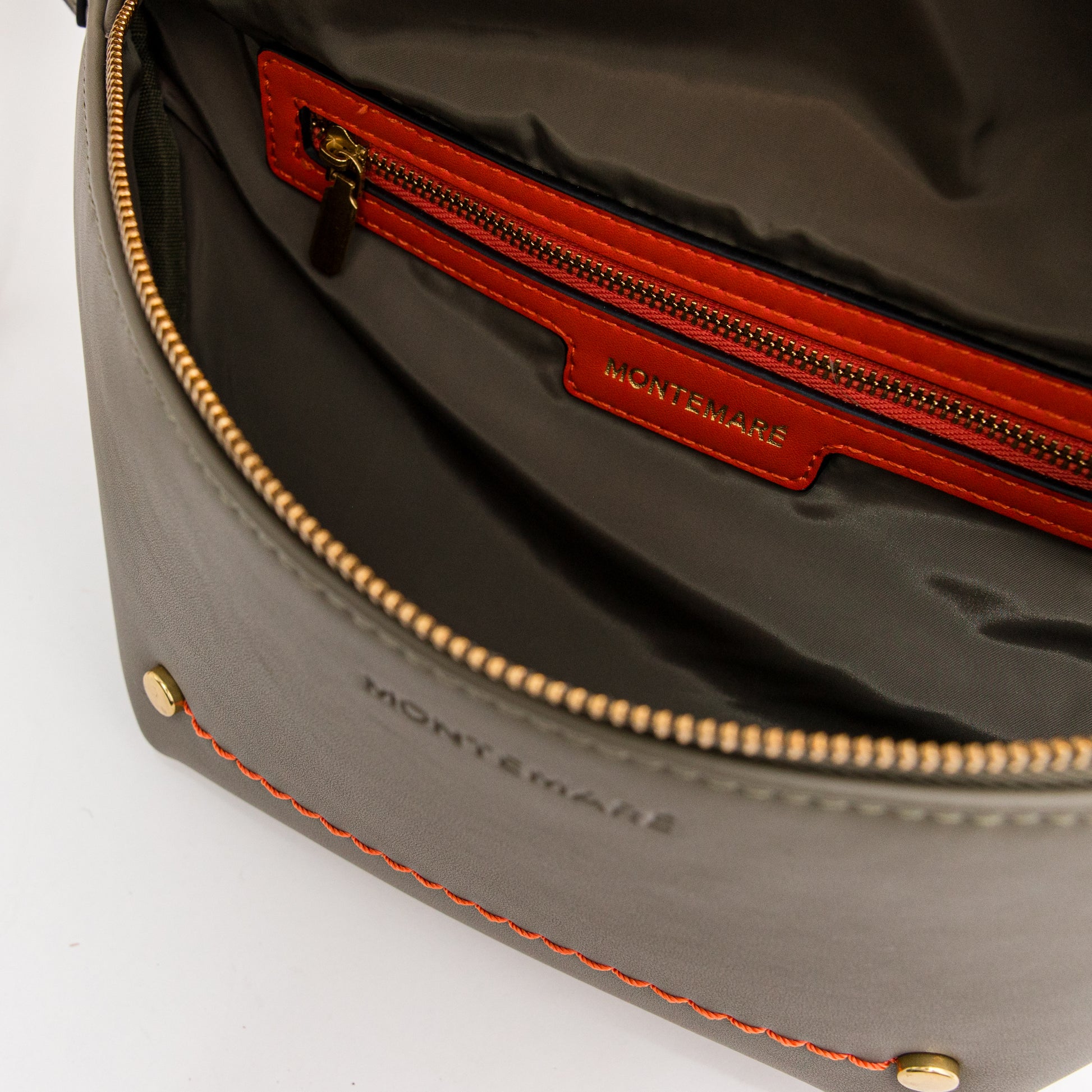 Close-up of an olive green vegan leather bag with brass-finished zipper and orange trim and stitching on a white background