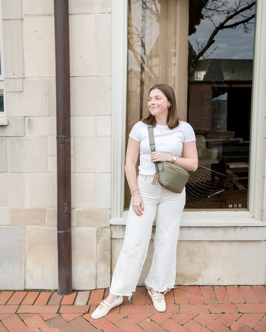 Montemaré Roma Sling in olive vegan leather worn crossbody by a woman in a white outfit on a city sidewalk