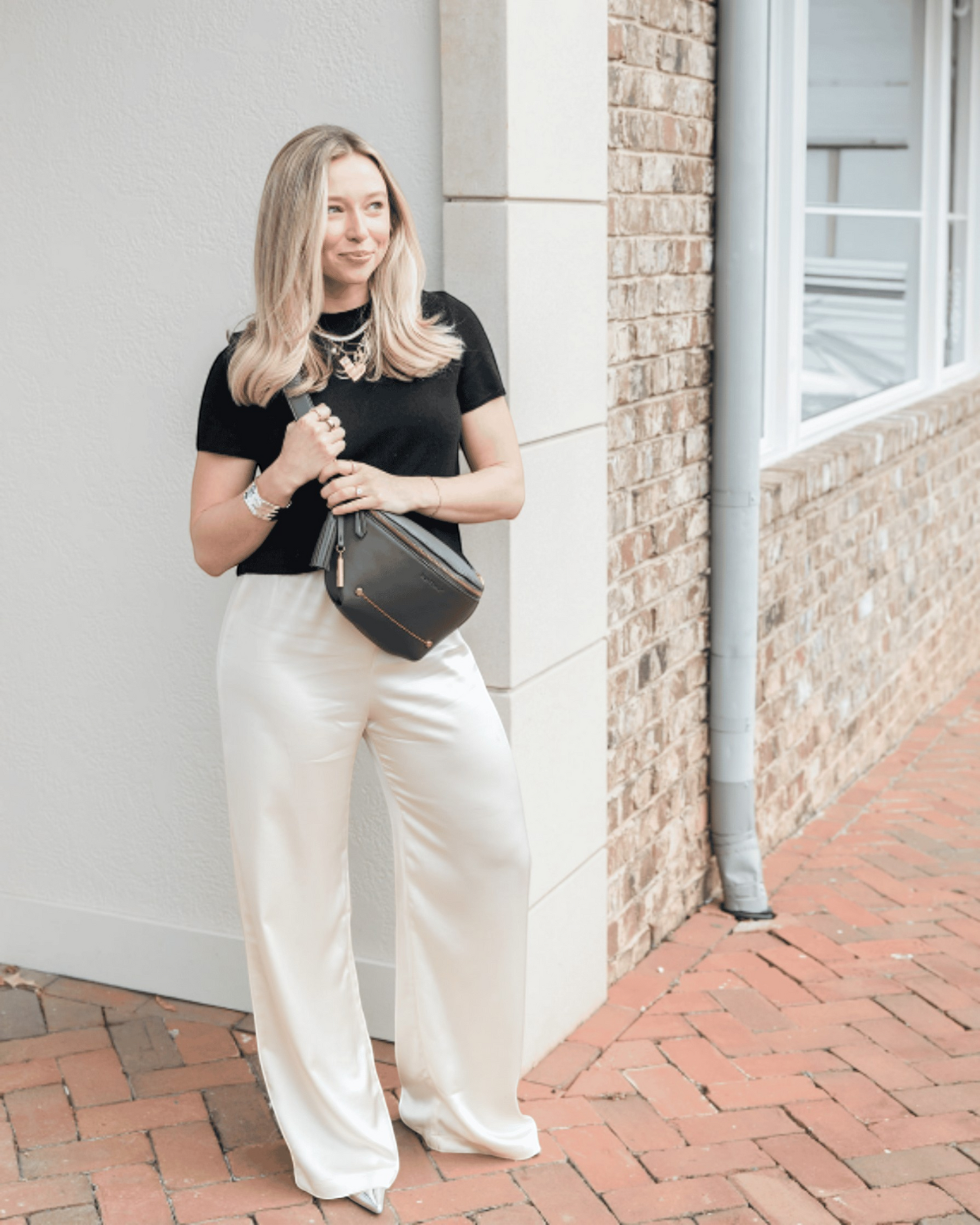 Woman wearing a black Montemaré Roma Sling vegan leather crossbody bag with a signature safety whistle tassel.