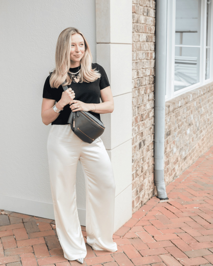Woman wearing a black Montemaré Roma Sling vegan leather crossbody bag with a signature safety whistle tassel.