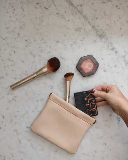 Montemaré Roma Square Pouch in beige vegan leather with spring-frame closure, shown with makeup brushes and compacts.