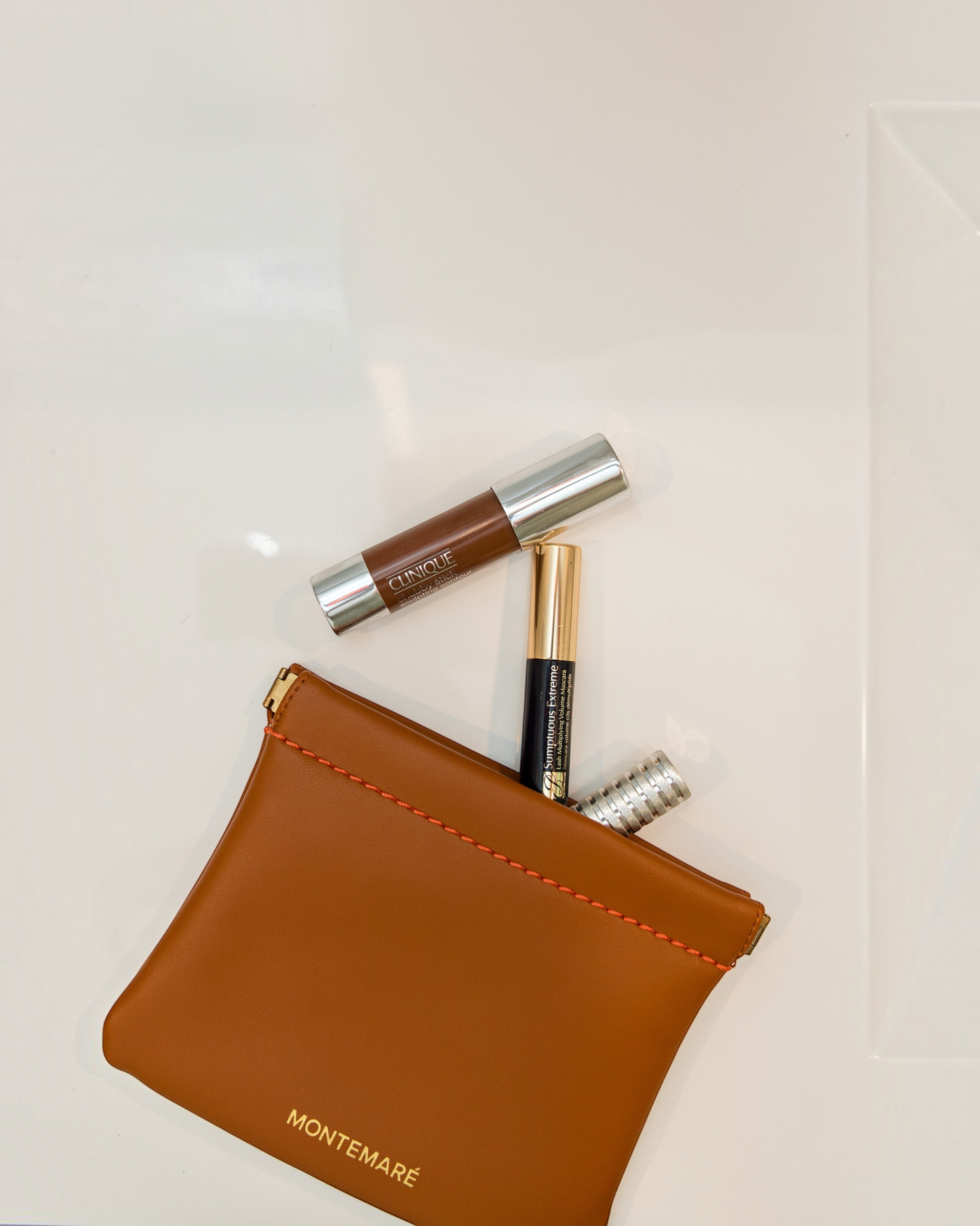 Montemaré Roma Square Pouch in tan vegan leather with spring-frame closure, holding makeup essentials on white surface