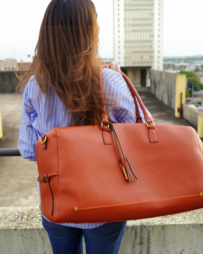 Woman carrying a tan Montemaré Roma vegan leather duffel bag with a tassel detail on a rooftop setting.
