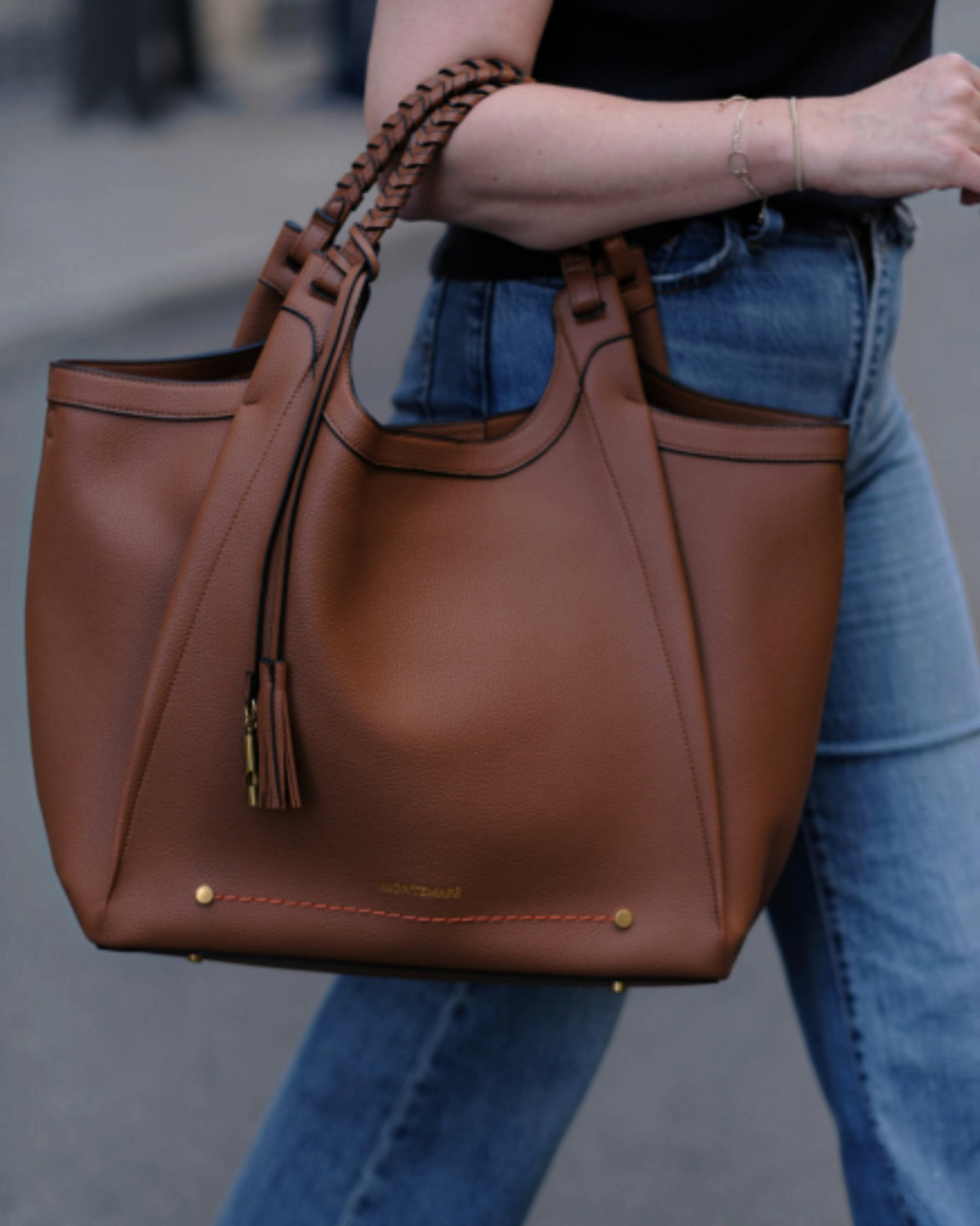 Montemaré Sedona work tote in brown vegan leather with hand-braided handles and signature tassel, carried by a woman.