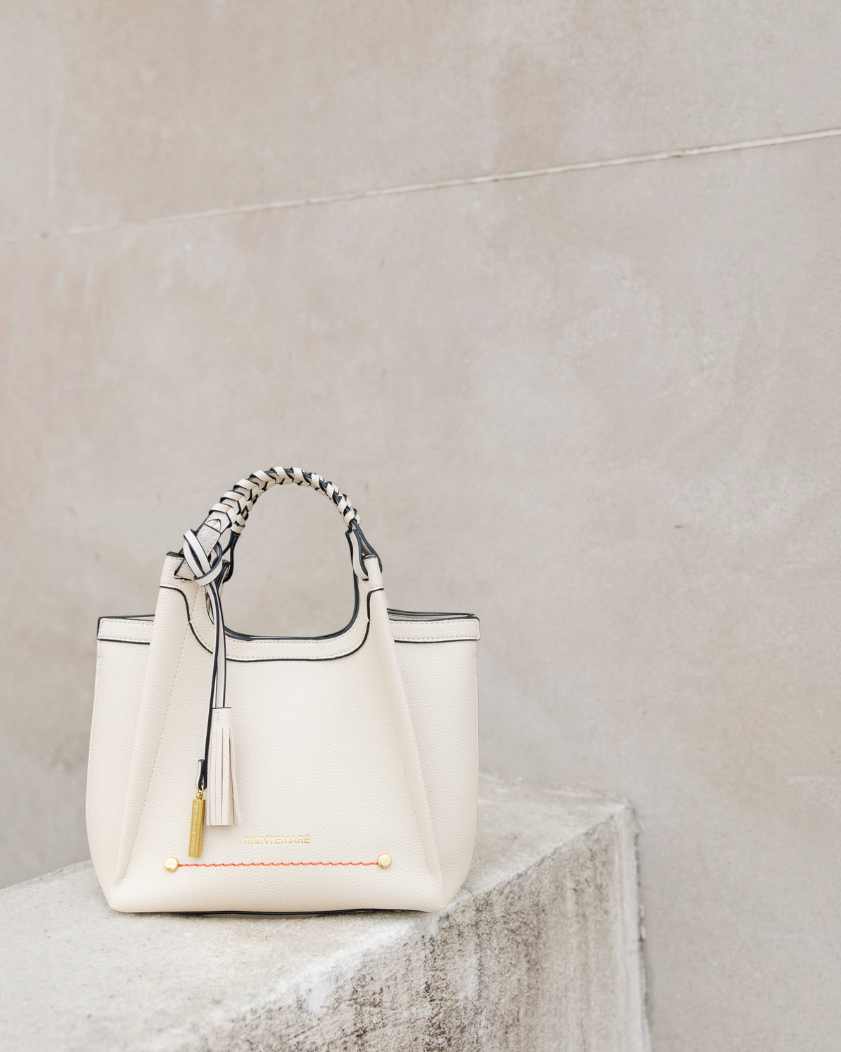Montemaré Sedona crossbody bag in cream pebbled vegan leather with a braided top handle and signature whistle tassel.