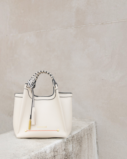 Montemaré Sedona crossbody bag in cream pebbled vegan leather with a braided top handle and signature whistle tassel.
