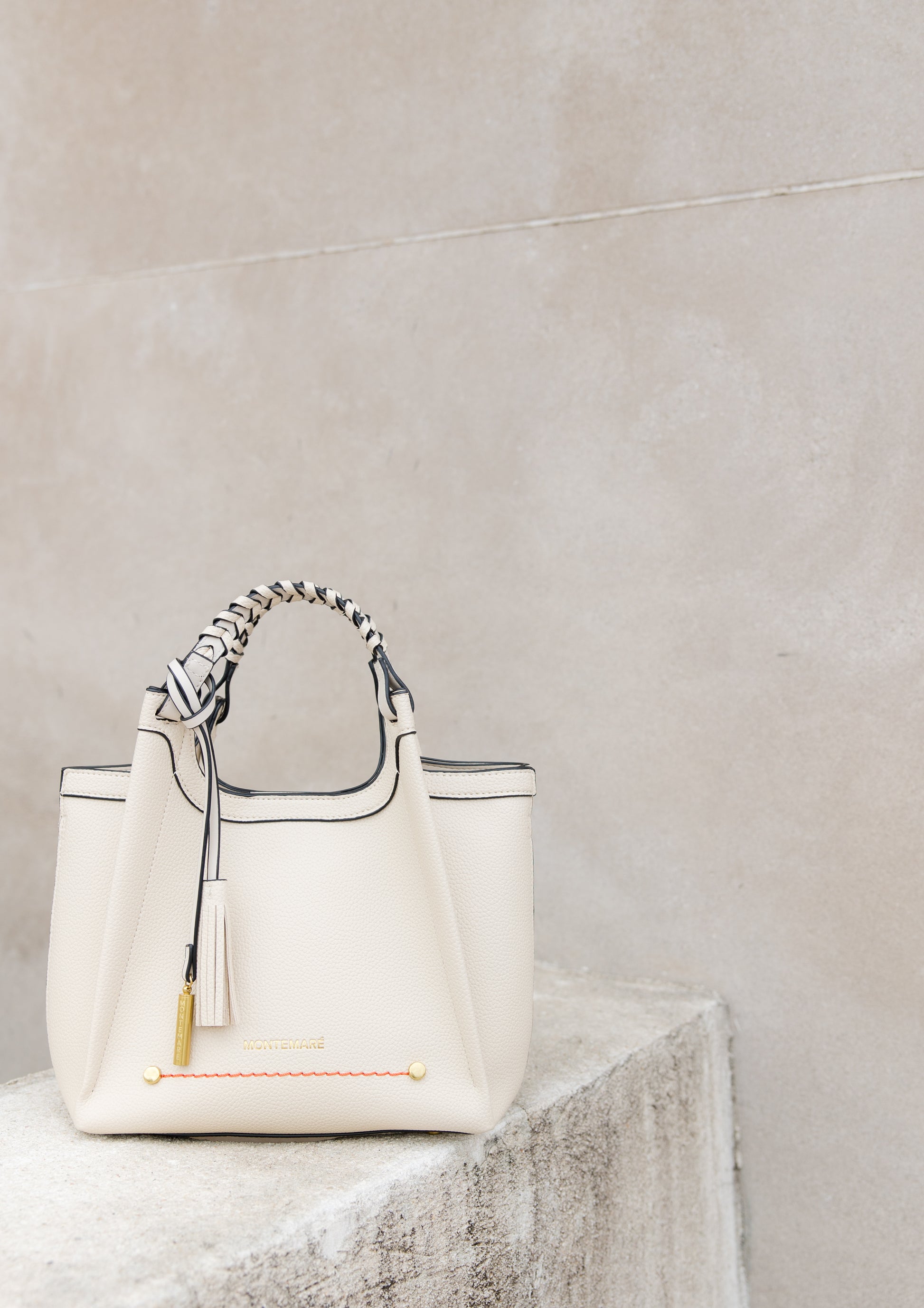 Sedona Crossbody in Ivory perched on cement wall with the safety whistle tassel hanging from the braided handle.