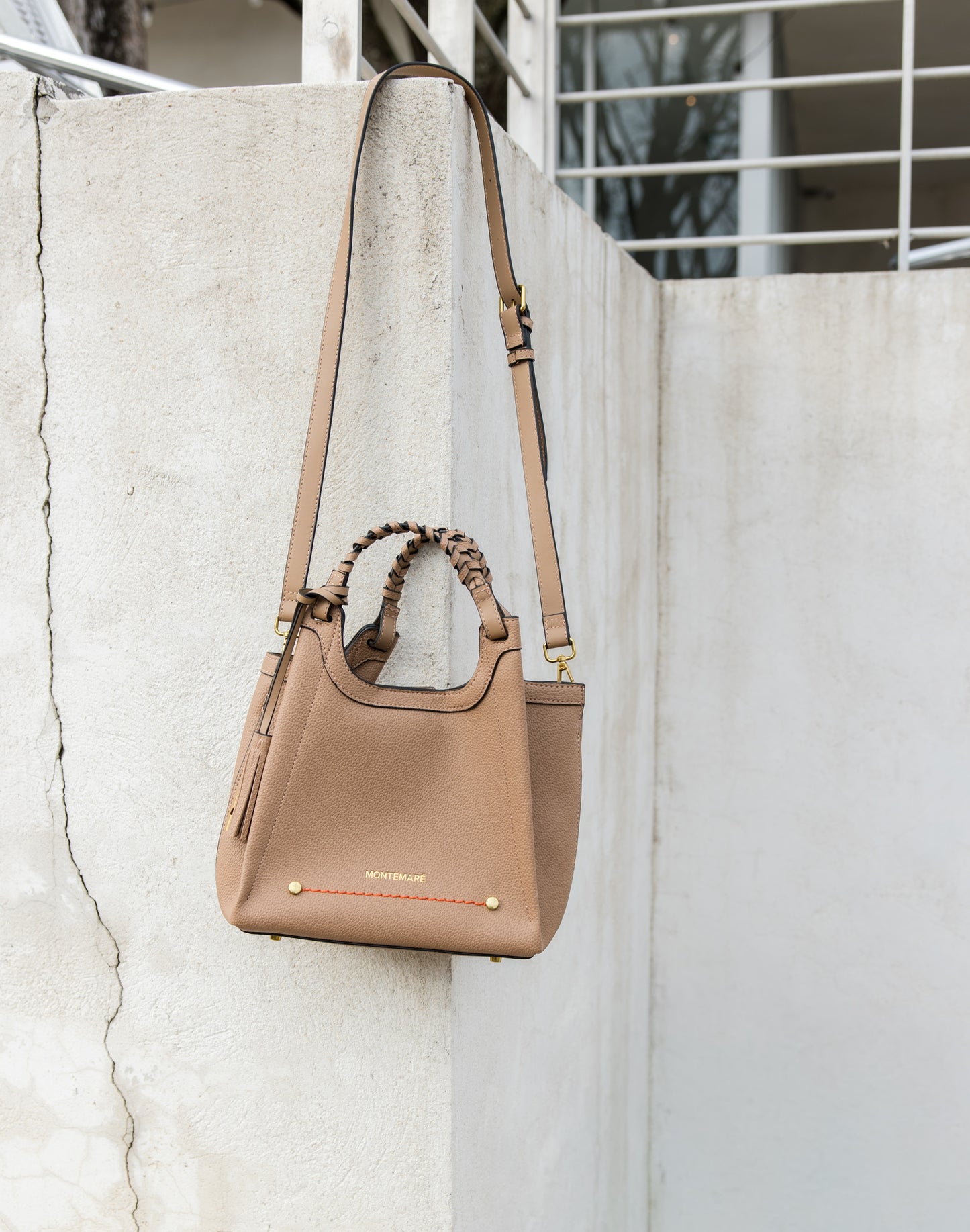 Sedona Crossbody in Latte hanging from wall from its crossbody strap, with the light showing off the orange journey line and metal feet.
