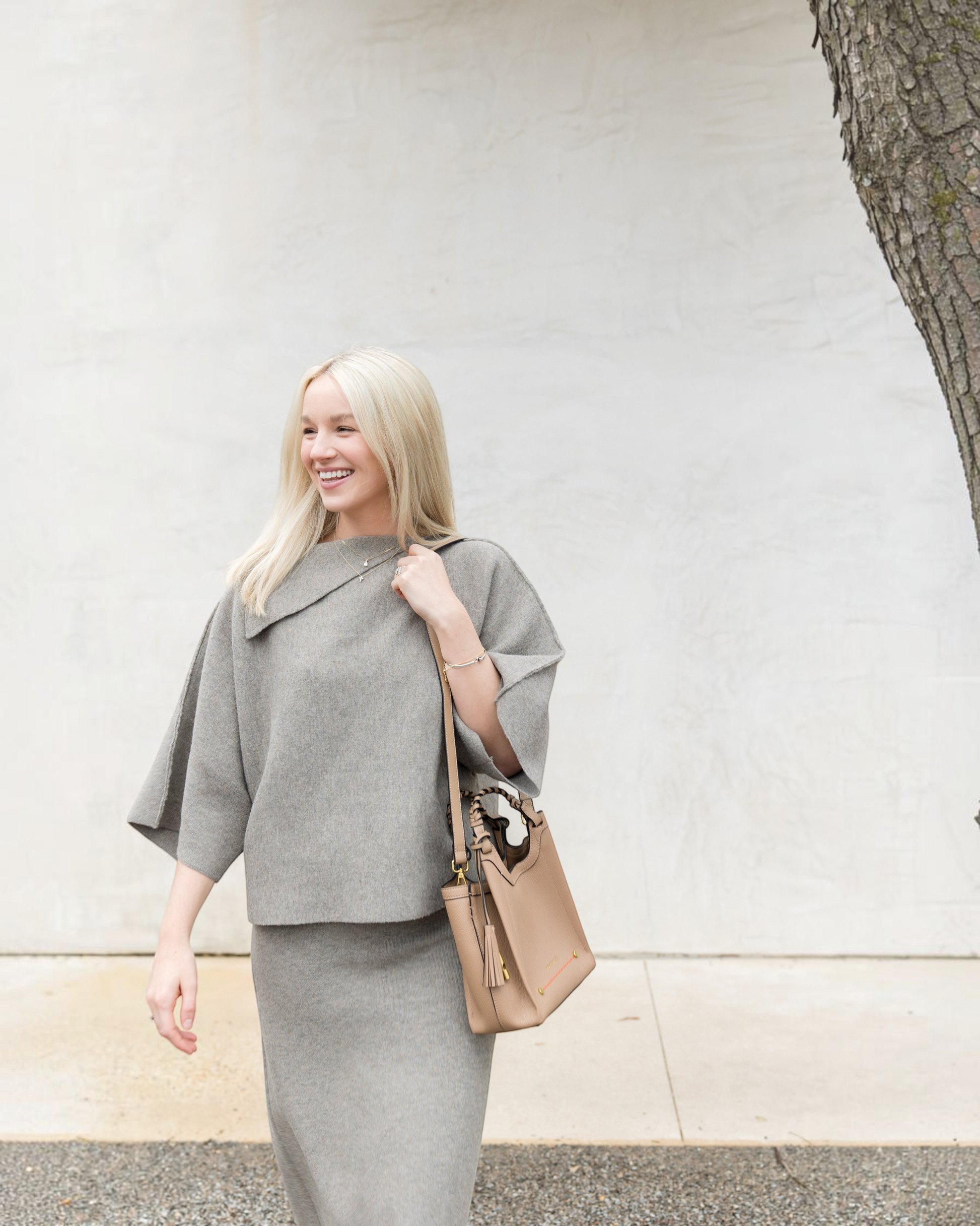 A woman wearing a grey outfit carries a Montemaré Sedona Crossbody bag made of tan pebbled vegan leather.