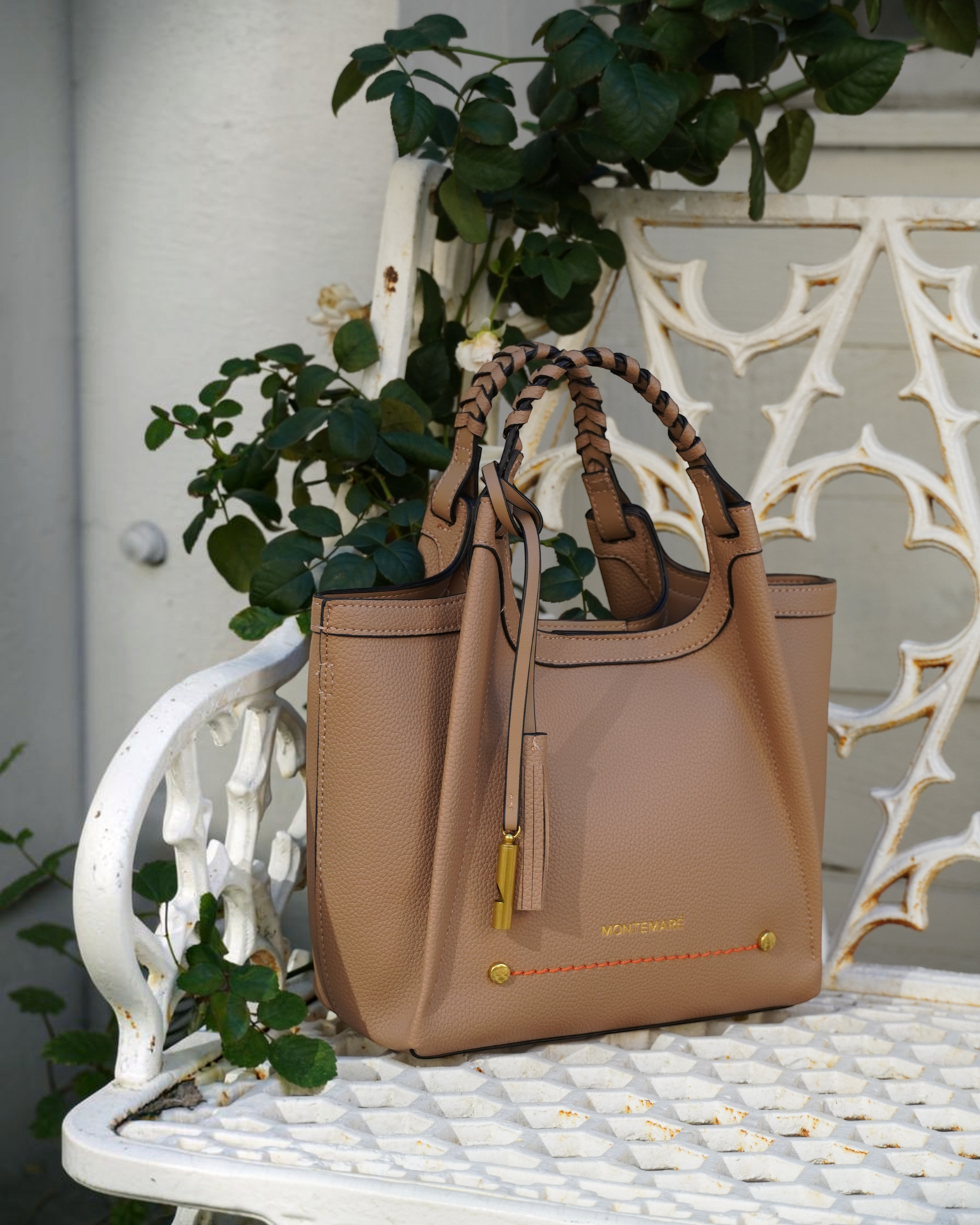 Montemaré Sedona Crossbody in tan pebbled vegan leather with a braided handle and signature whistle tassel on a bench.