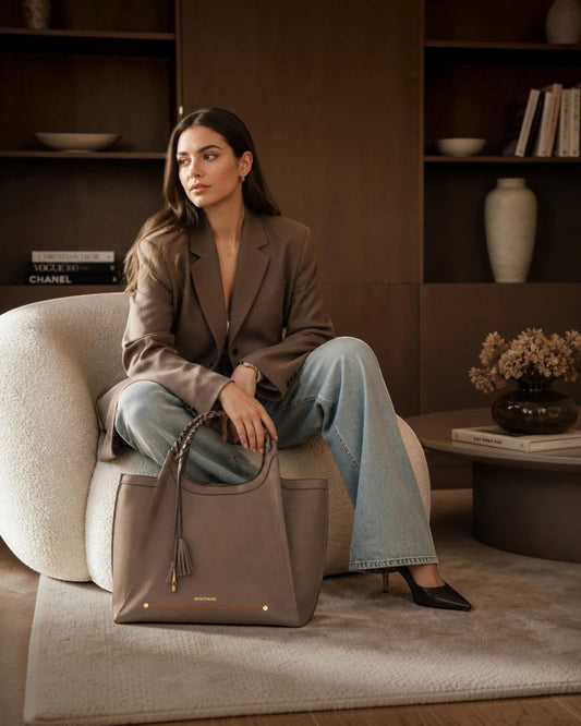Woman sitting in a chair holding a Montemaré Sedona Work Tote in pebbled brown vegan leather with braided handles.