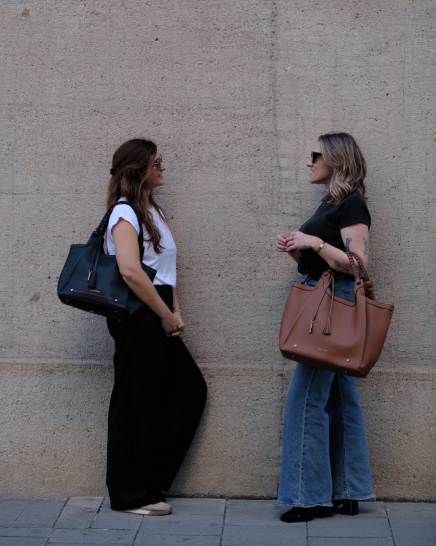 Two women standing outdoors carrying Montemaré Sedona Work Totes in black and tan vegan leather with braided handles.