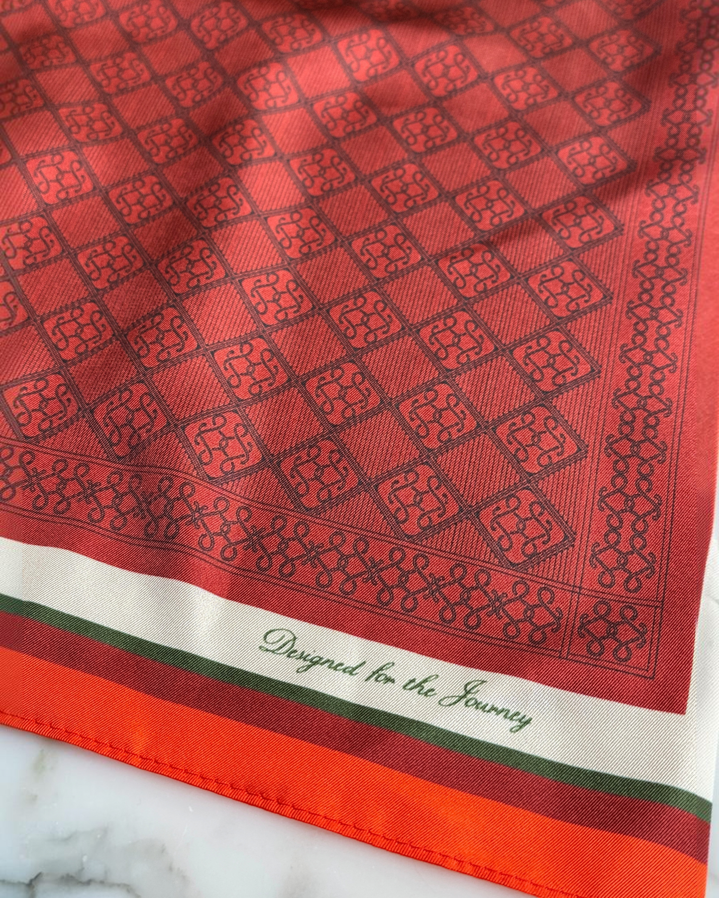 Montemaré Original Silk Square Scarf in red with a signature grid pattern and Designed for the Journey text detail.