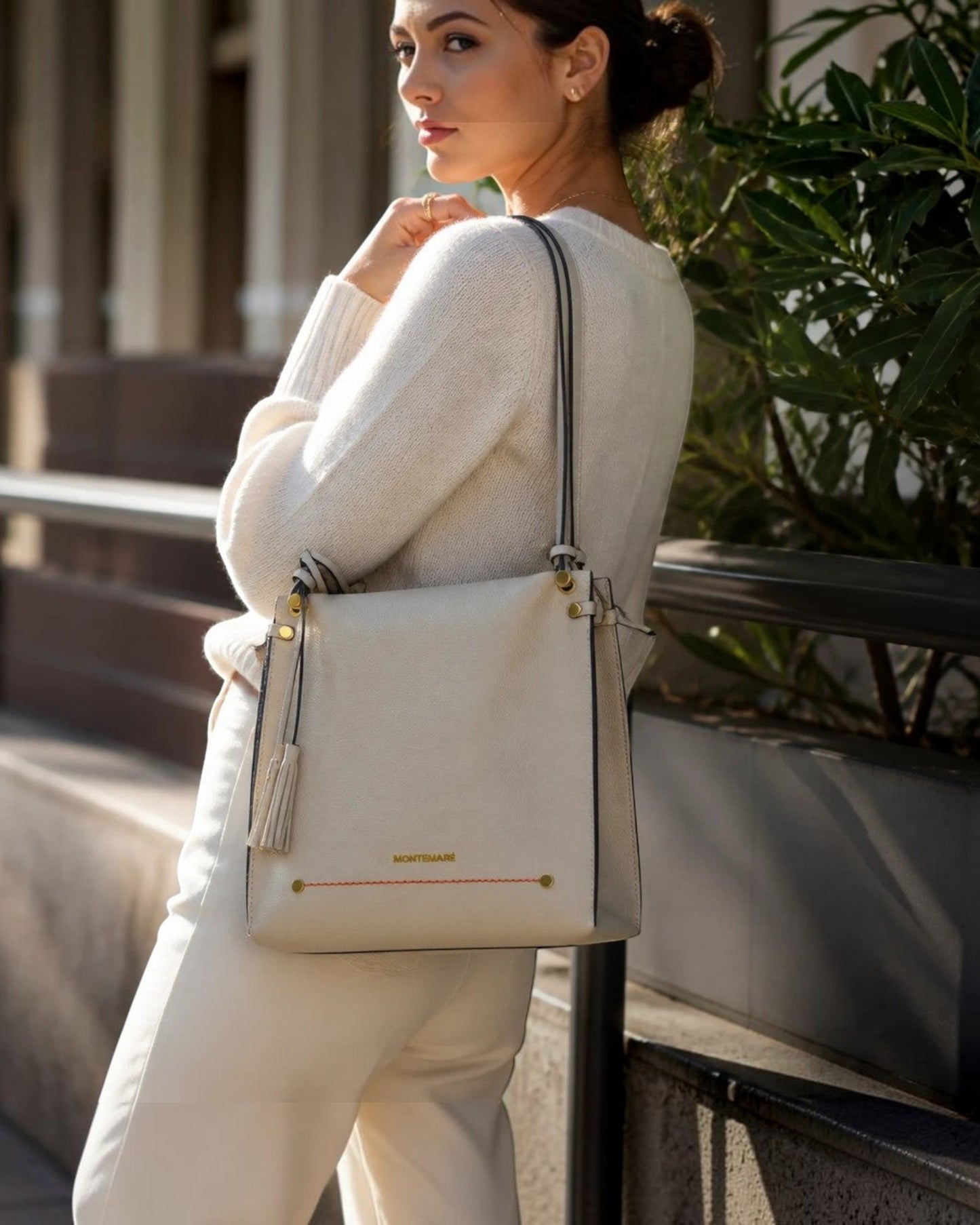 Montemaré Vienna shoulder bag in cream pebbled vegan leather with a signature whistle tassel worn by a woman