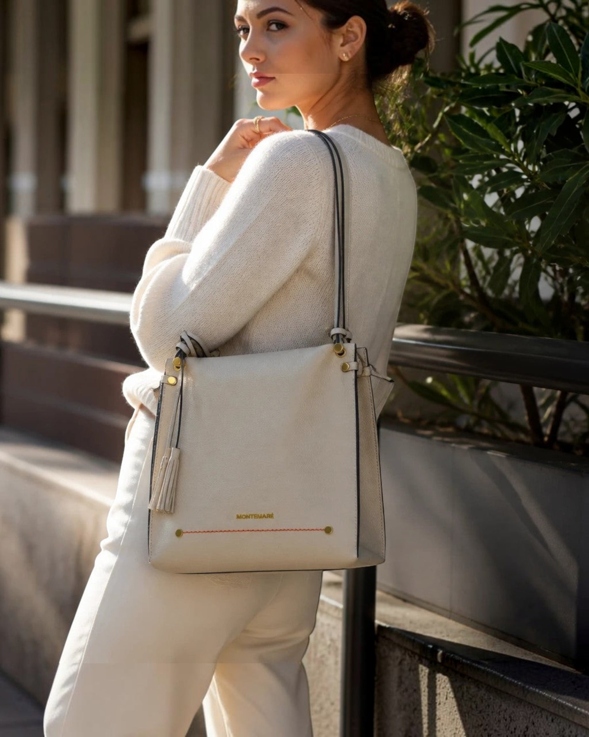 Montemaré Vienna shoulder bag in cream pebbled vegan leather with a signature whistle tassel worn by a woman