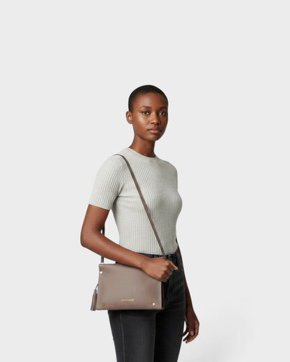 Model wearing a taupe Montemaré Vienna Crossbody bag made of pebbled vegan leather with a signature whistle tassel.