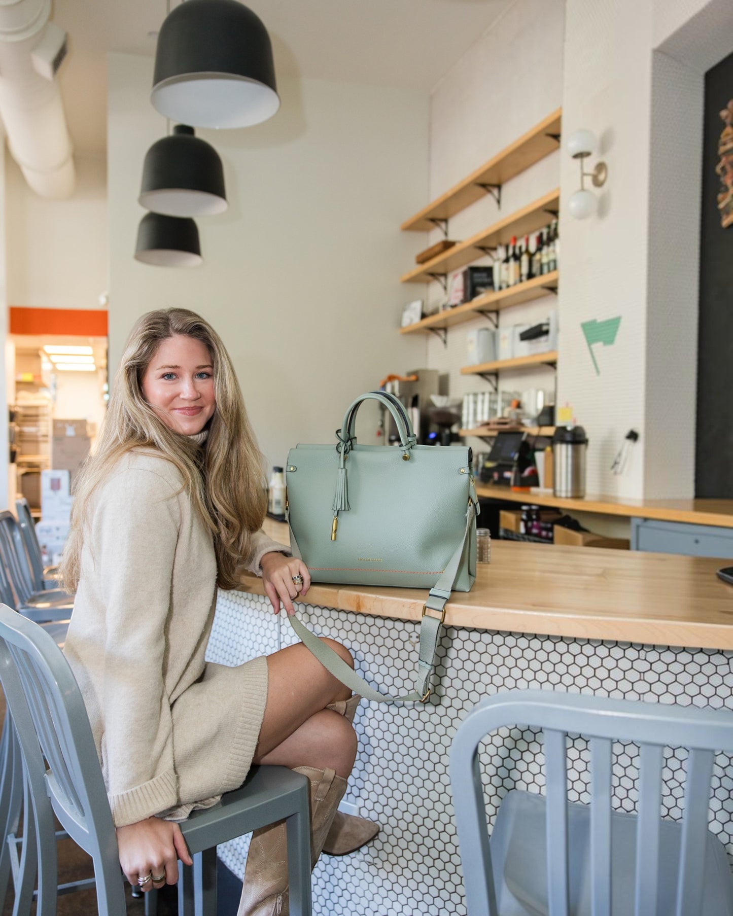 Woman sitting at a cafe counter with a sage green Montemaré Vienna vegan leather carry-on tote bag.