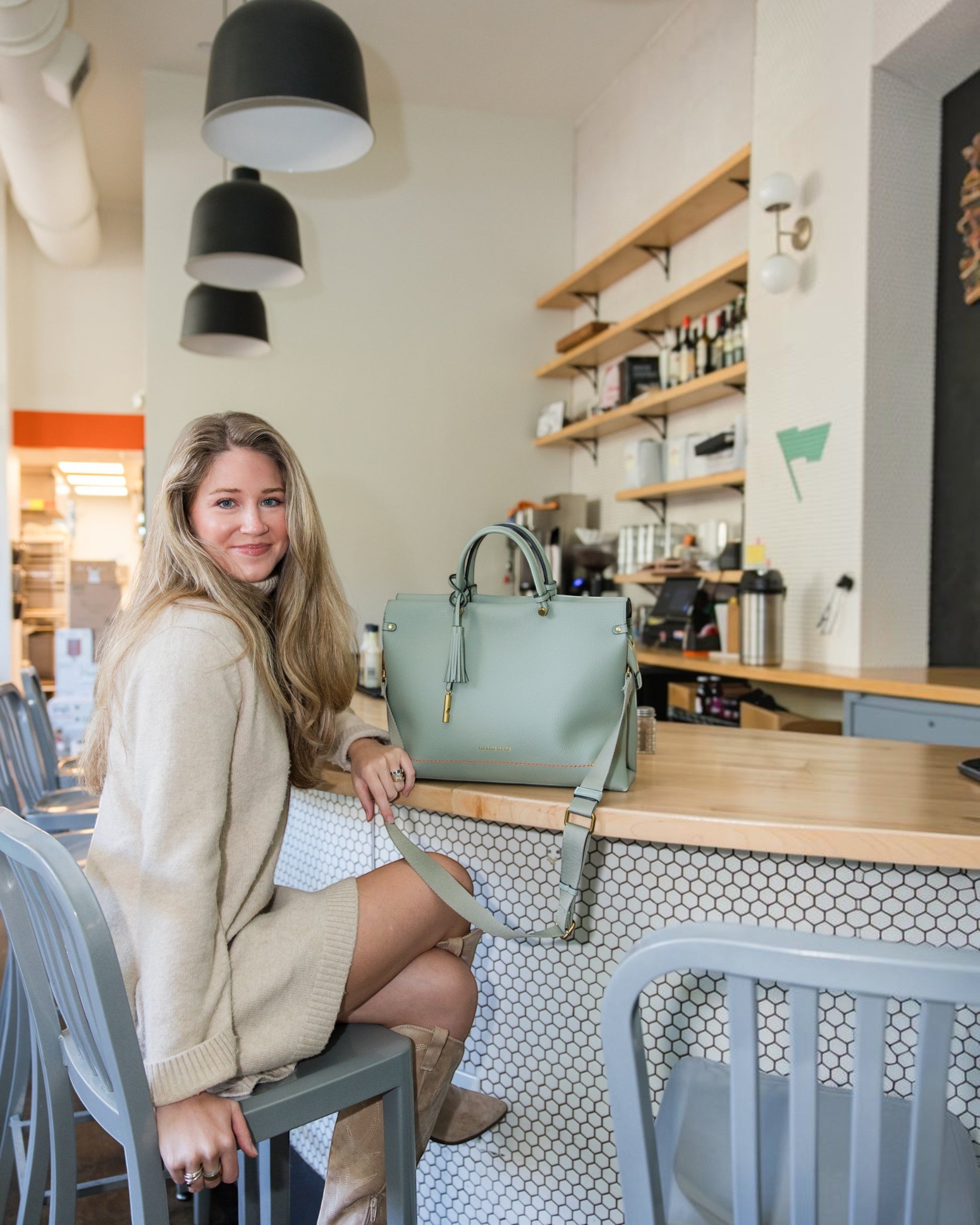 Woman sitting at a cafe counter with a sage green Montemaré Vienna vegan leather carry-on tote bag.
