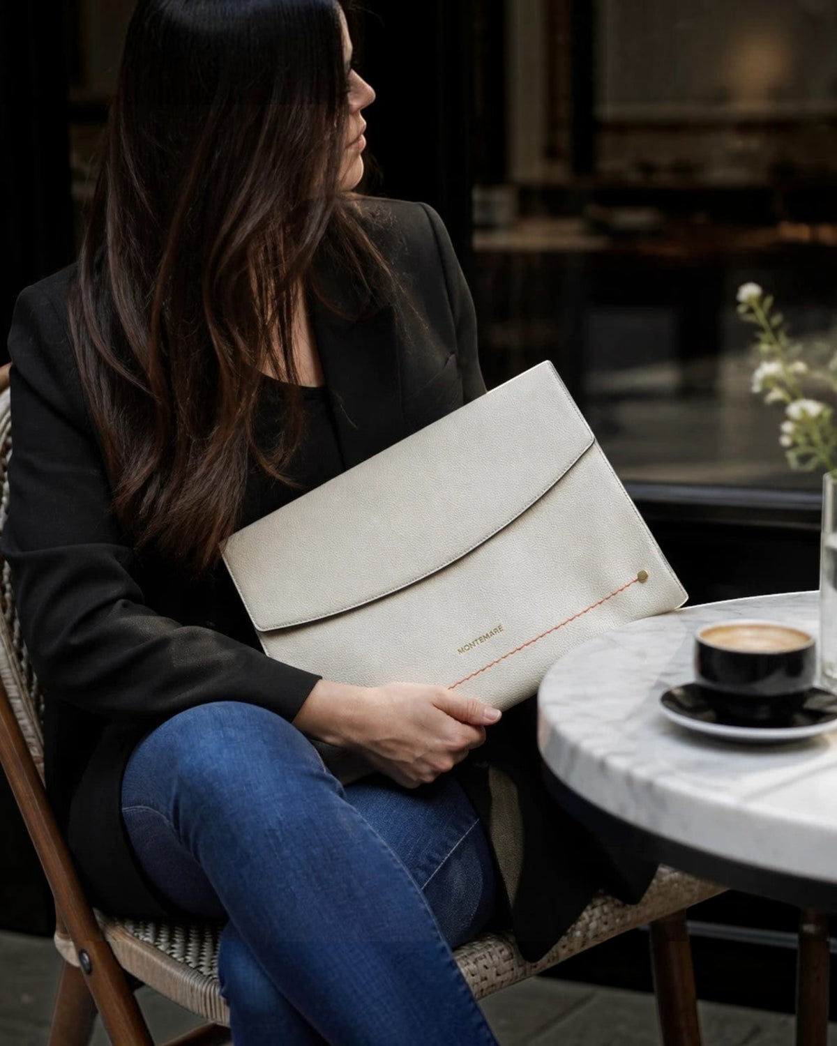 Montemaré Vienna laptop case in off-white vegan leather held by a woman in a blazer at a cafe table.